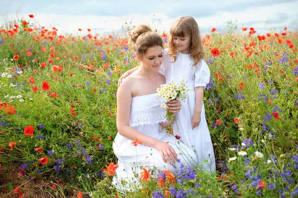 kind dochter knuffelen van haar moeder onder de bloemen van het veld - Foto, afbeelding