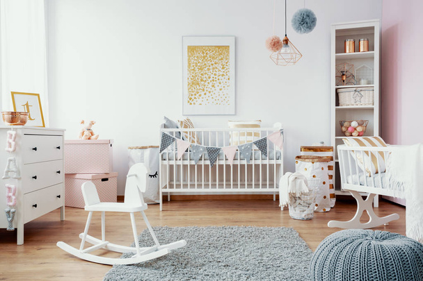 Bright baby room with white furniture, grey carpet on the floor and golden painting on the empty wall, real photo - Foto, imagen