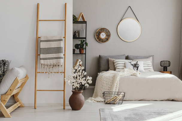 Scandi open space bedroom interior with double bed with knit blanket and many pillows, rack with books and decor, carpet on the floor in real photo - Valokuva, kuva