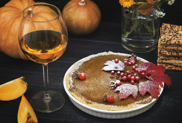 Two glasses of white wine, pumpkin pie with viburnum berries on the background of pumpkins, autumn leaves and black wooden background - Photo, Image