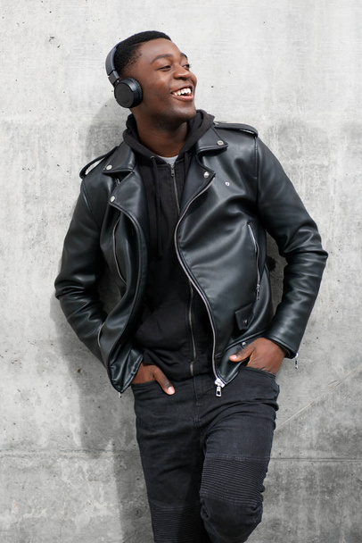 Πορτρέτο του χαμογελώντας μαύρος σε δερμάτινο σακάκι, να ακούτε μουσική με ακουστικά - Φωτογραφία, εικόνα
