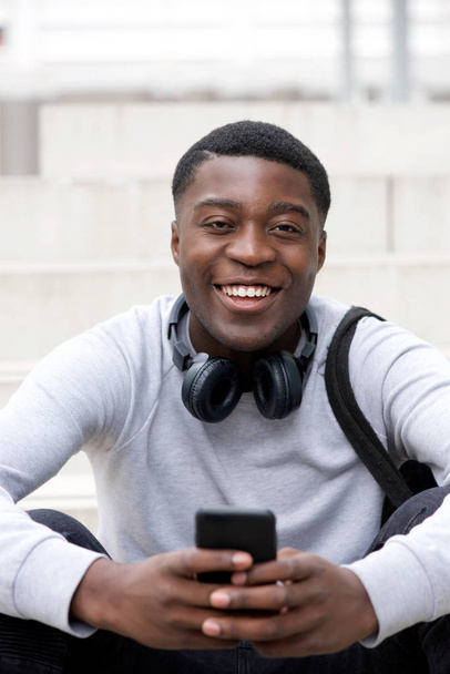 Portret fajny młody czarny człowiek uśmiechnięty telefon i słuchawki - Zdjęcie, obraz