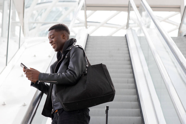 Ritratto di giovane nero con cellulare e borsa su scala mobile alla stazione
 - Foto, immagini