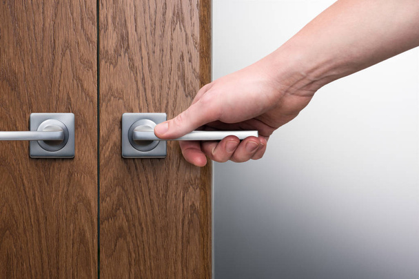 A man's hand on a steel door handle. Swinging interior door. Dark oak texture. Frosted glas - Φωτογραφία, εικόνα