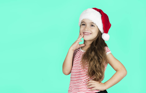 Little bright beautiful girl emotionally posing in Santa hat on an isolated turquoise background - Fotó, kép