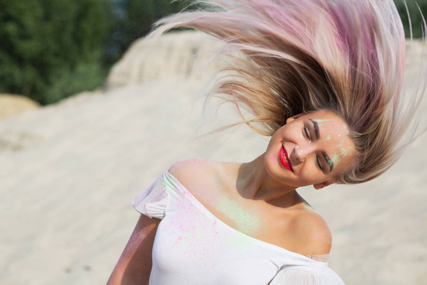 Joyful blonde girl with fluttering hair covered with dry paint Holi at the desert. Space for text - Фото, зображення