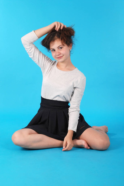 Молода дівчина сидить на підлозі на синьому фоні в студії
. - Фото, зображення