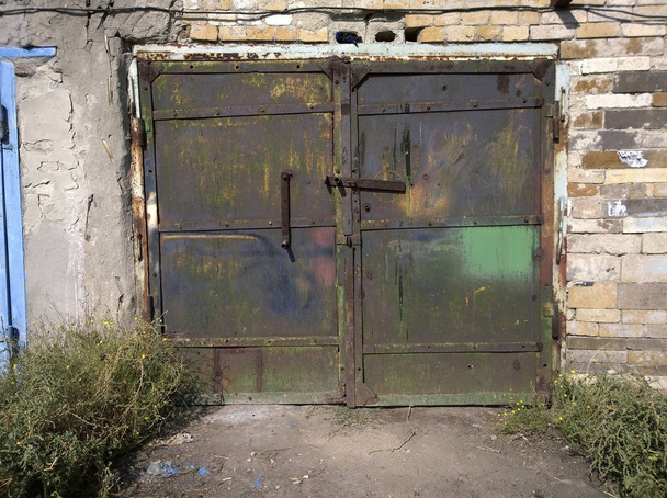 Portas de garagem dupla de metal velho com tinta de descascamento em sua superfície, fechadas com uma trava de parafuso
 - Foto, Imagem