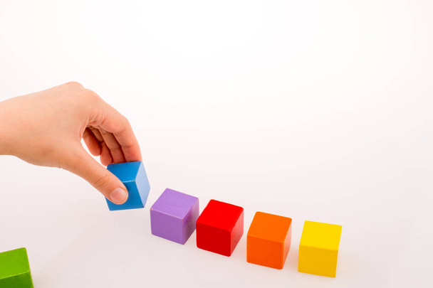 Hand spelen met kleurrijke blokjes op een witte achtergrond - Foto, afbeelding