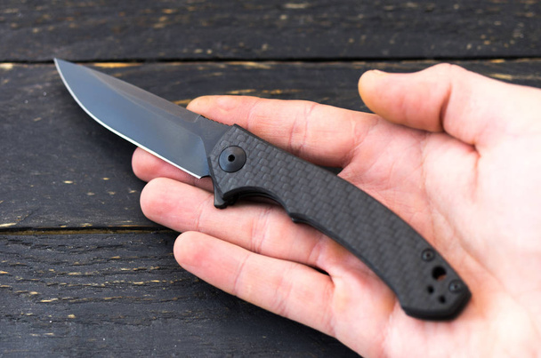 Black pocket knife in hand. Knife in the right hand. Compact pocket knife. - Photo, Image