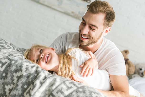 happy father hugging adorable little daughter on bed - Fotó, kép