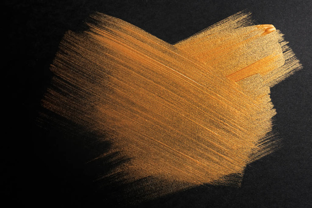 Slagen van gouden verf op een donkere achtergrond - Foto, afbeelding
