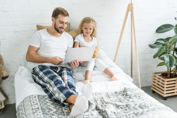 wysoki kąt widzenia szczęśliwy ojciec i córka trochę za pomocą laptopa ze sobą na łóżku - Zdjęcie, obraz