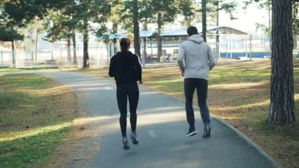Taustalla kaunis pari mies ja nainen käynnissä puistossa yhdessä yllään trendikäs urheiluvaatteet ja lenkkarit. Aktiivinen nuoriso, terveet ihmiset ja vapaa-ajan käsite
. - Materiaali, video