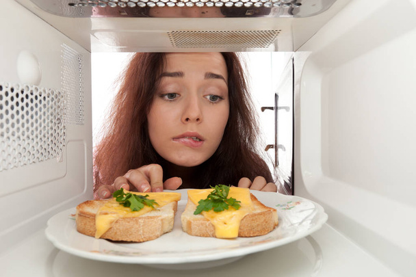 Attractive girl looking in a microwave - Foto, imagen
