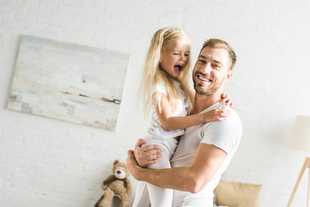 ευτυχισμένος πατέρας και η αξιολάτρευτη μικρή κόρη αγκαλιάζει στο σπίτι - Φωτογραφία, εικόνα