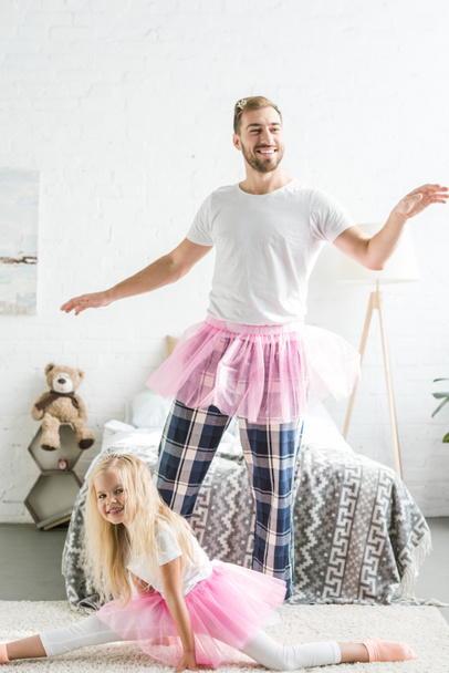 happy father and daughter in pink tutu skirts having fun and dancing together at home - Foto, imagen