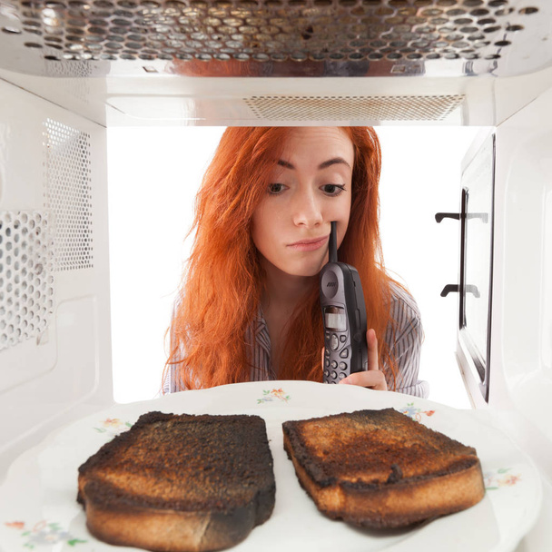 Girl looking to a burned toasts in microwave - Foto, afbeelding