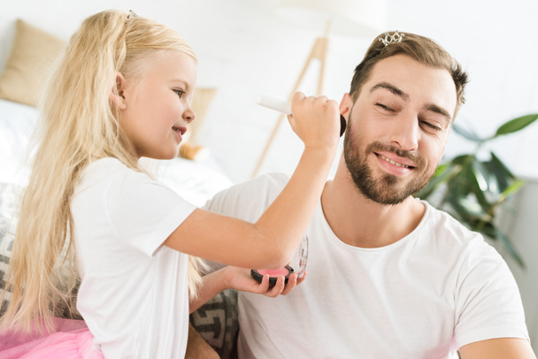 cute little daughter applying makeup to happy bearded father at home    - Fotó, kép