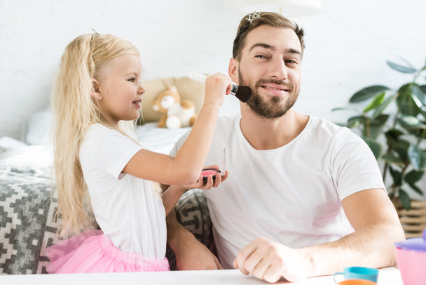 linda hijita aplicando maquillaje a padre feliz en casa
   - Foto, Imagen