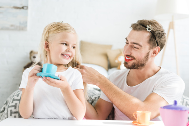happy father plaiting braid to adorable daughter pretending to have tea party at home  - Foto, Bild