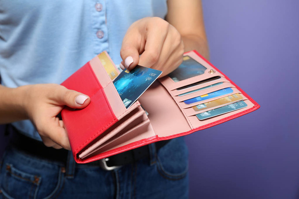 Young woman holding wallet with credit cards on color background, closeup - Photo, Image