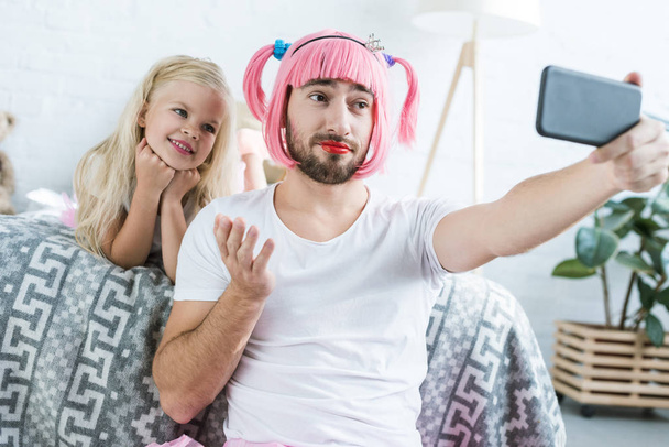 happy little daughter and father in pink wig taking selfie with smartphone at home - Φωτογραφία, εικόνα