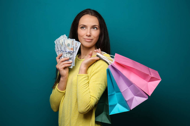 schönes Mädchen mit Einkaufstaschen und viel Geld auf farbigem Hintergrund - Foto, Bild