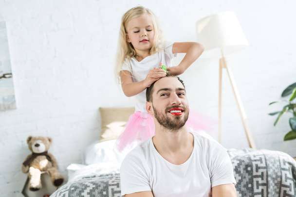 cute little daughter in pink tutu skirt playing with happy father with red lipstick  - Φωτογραφία, εικόνα