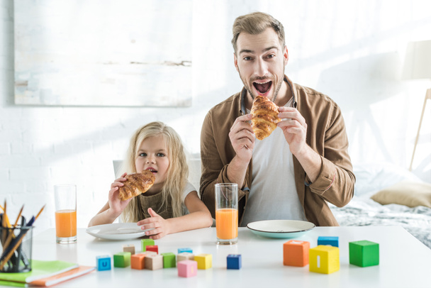 Vater und Tochter essen Croissants und schauen in die Kamera - Foto, Bild
