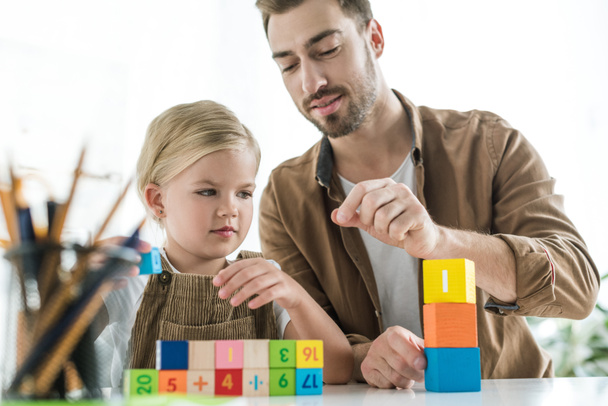 father explaining math to little daughter and playing with colorful cubes at home - Fotó, kép