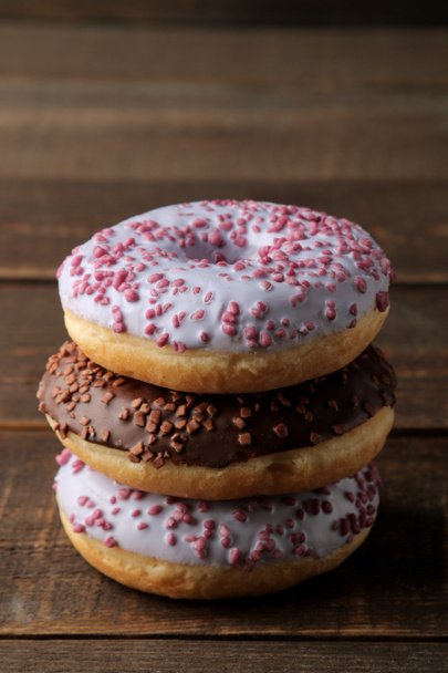 Assorted sweet donuts stacked on a brown wooden table with icing and sprinkling. - Foto, imagen