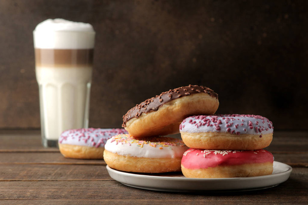 Donuts doces variados com cobertura e cobertura, e café latte em uma mesa de madeira marrom
. - Foto, Imagem