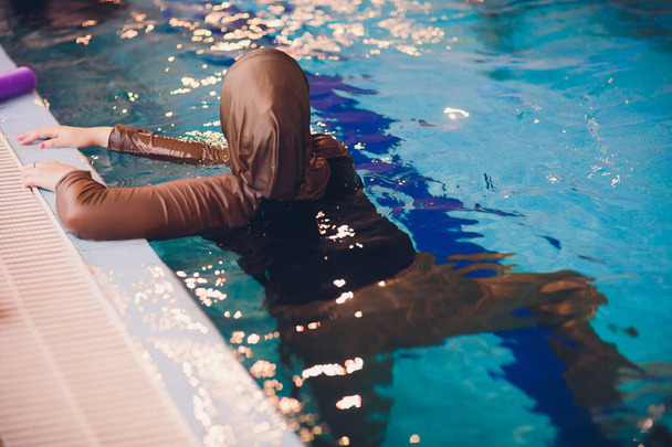 Young muslim girl swimming at pool brown clothes. - Фото, зображення