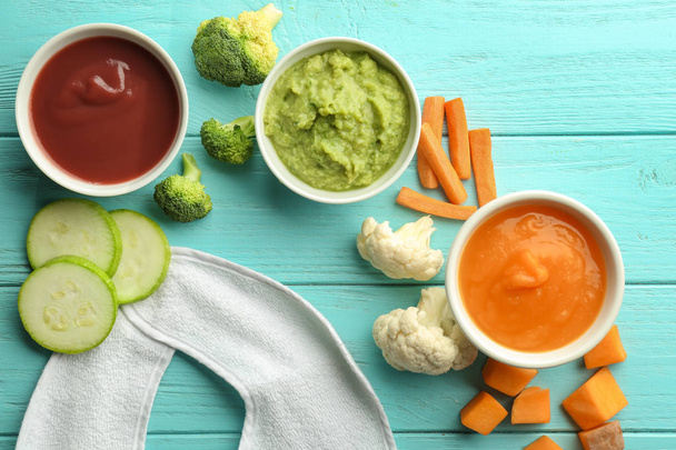 Bowls with healthy baby food and ingredients on color wooden table - Foto, imagen