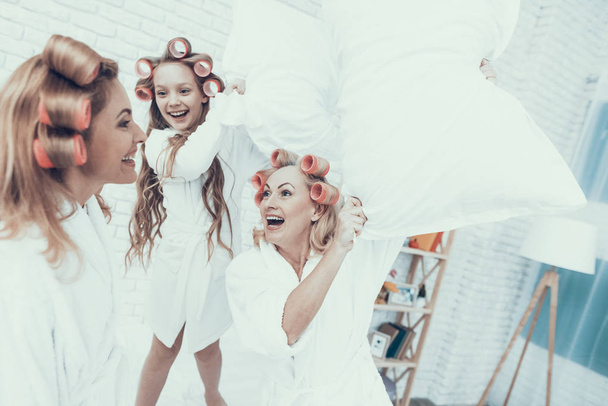Smiling Women in White Bathrobes Have Fun at Home. Happy Family. Mother with Daughter. Smiling Women. Smiling Grandmother. Have Fun Indoor. White Sofa. Family after Bath. Pillow Fight. - Foto, Imagem