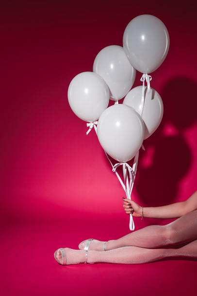 cropped image of girl sitting and holding bundle of white balloons at party on burgundy - Foto, afbeelding
