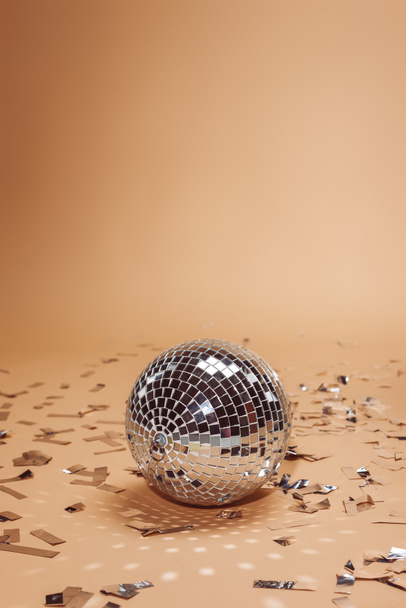 shiny silver disco ball and confetti on beige - Foto, afbeelding