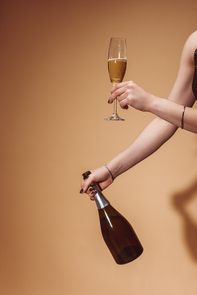 cropped image of woman holding glass and bottle of champagne at party on beige - Valokuva, kuva