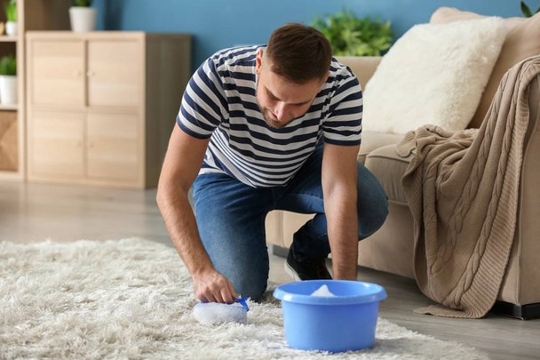 Young man cleaning carpet at home - Foto, afbeelding