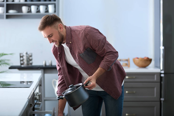 Nuori mies laittaa kattilaan kaappiin, kun siivoat keittiötä
 - Valokuva, kuva