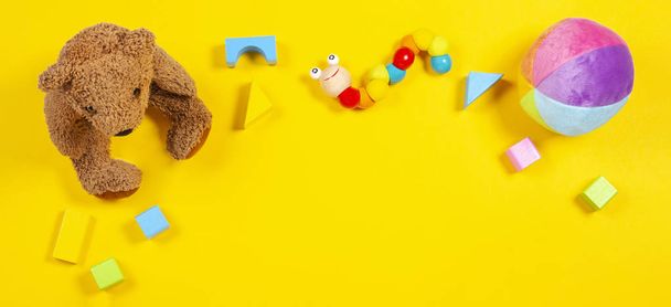 Baba gyerek játékok keret mackó, fa játék-autó, sárga háttér színes kockák. Szemközti nézet - Fotó, kép