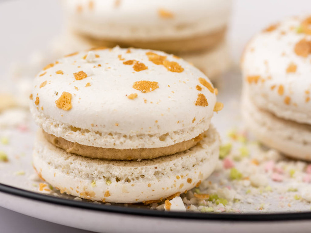 Three beige white macaroon cookies with multicolored crumb on white plate with blue border. Food background, shallow DOF, soft focus. - Foto, imagen