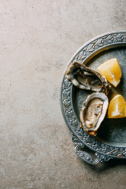 top view of oysters and lemon pieces on metal tray on grey tabletop - Foto, Imagen