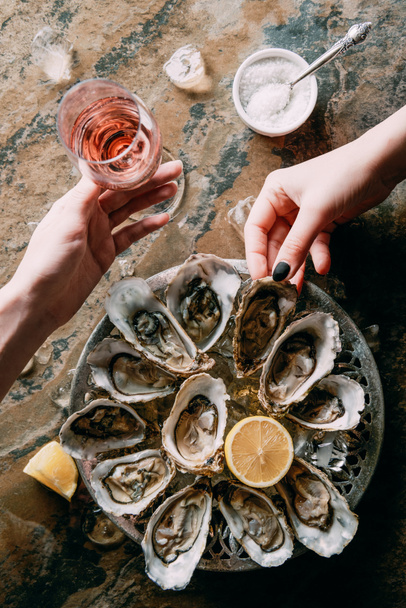partial view of women at grungy tabletop with glass of wine, oysters, ice and lemon - Foto, Imagem