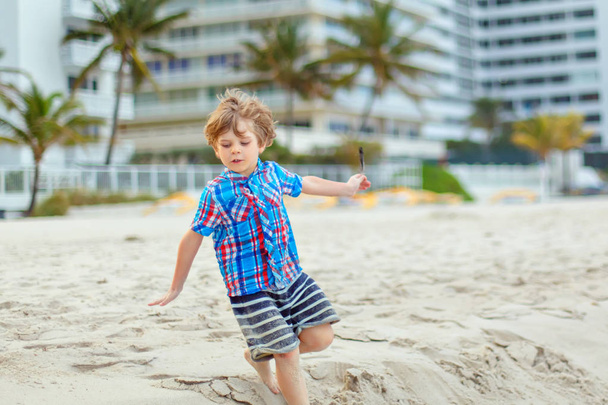 Ritratto di bambino felice sulla spiaggia dell'oceano. Divertente bambino carino fare vacanze e godersi l'estate. Ragazzo sano sulla spiaggia di Miami USA in un giorno tempestoso ventoso. - Foto, immagini