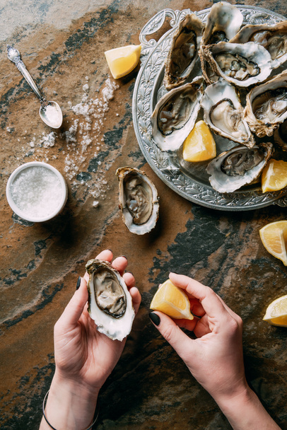 cropped shot of woman holding oyster and lemon piece in hand at grungy tabletop - Fotó, kép