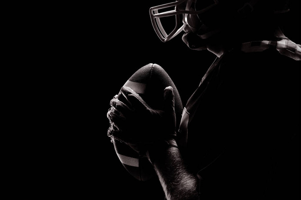 Side view of American football player standing with rugby helmet and ball - Фото, изображение