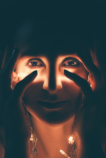 Portret van een vrouw met feestelijke verlichting camera kijken - Foto, afbeelding
