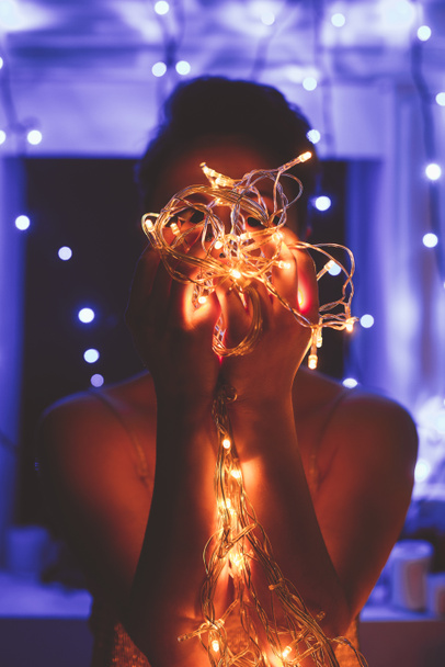 obscured view of woman holding festive lights in hands at home - Fotoğraf, Görsel